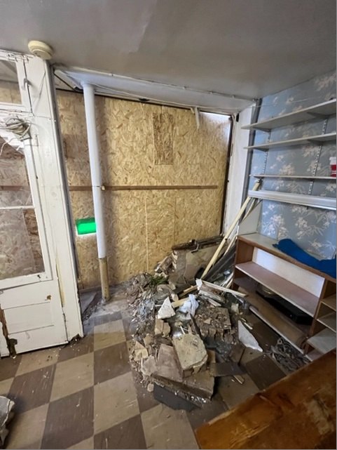 Boarded-up shopfront seen from inside, with fallen masonry on the chequered floor